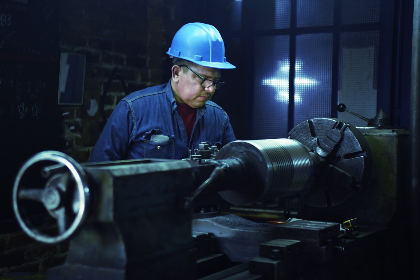 A machinist in a hard hat working at a lathe